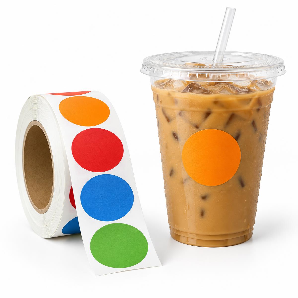 Rouleau de stickers ronds colorés à côté d'un gobelet transparent de café glacé avec un sticker orange